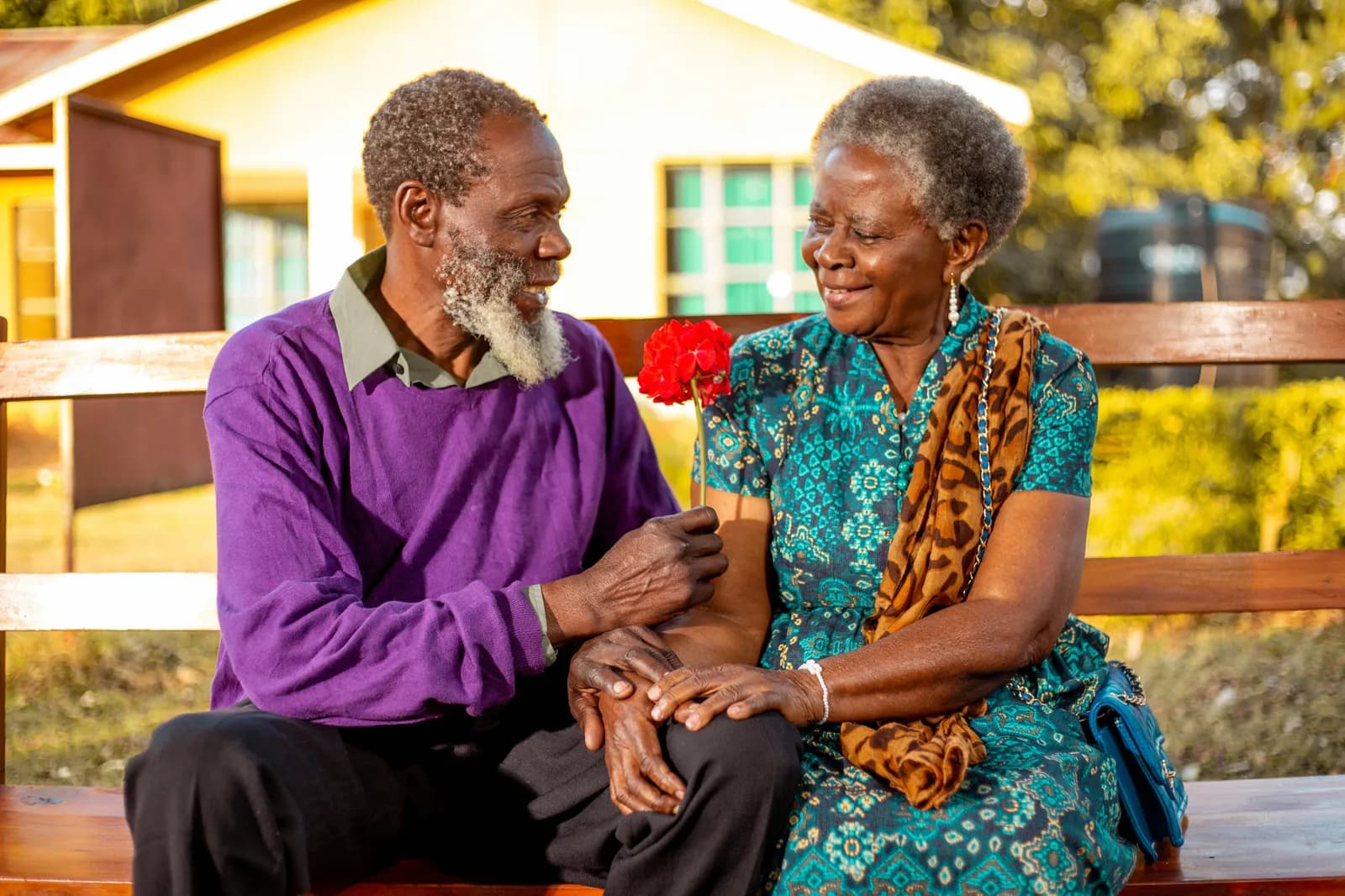 An older married couple sitting close on a bench outside their home, one handing the other a red flower — a spouse caregiver in Indiana