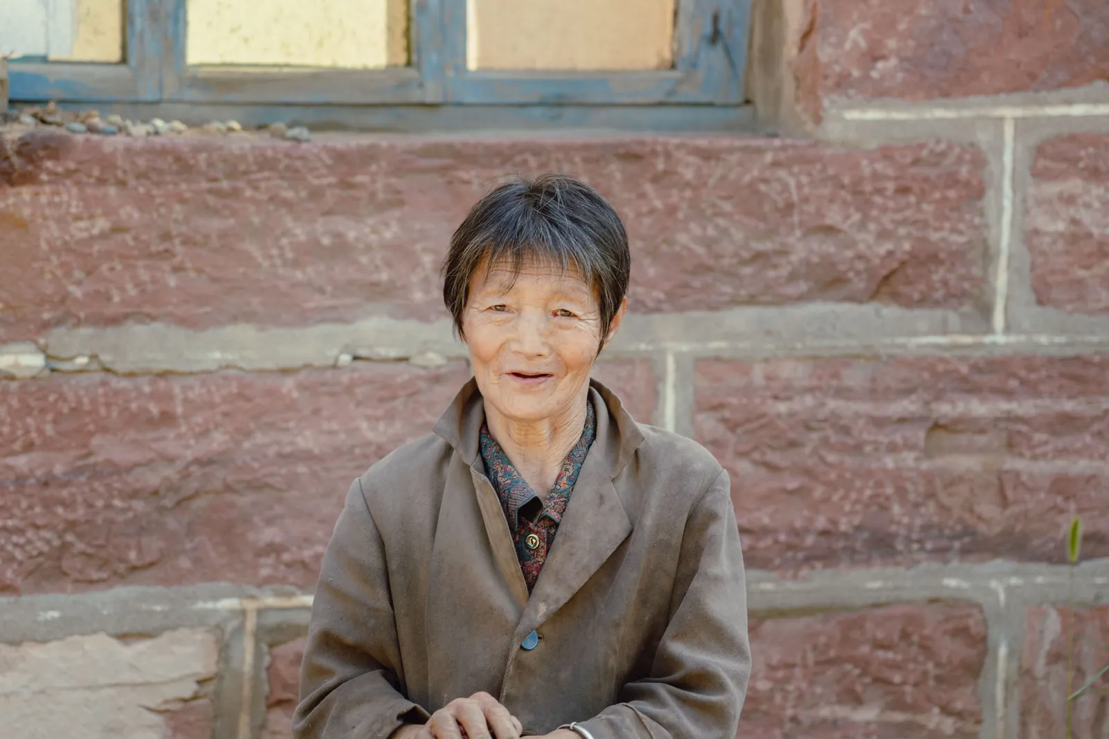 A warm older woman sitting outside a stone home, the kind of care recipient whose assessed needs set the Indiana SFC payment level